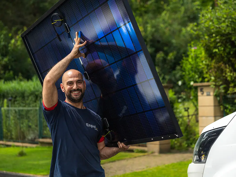 Ein Infravoltaic Handwerker trägt ein Solarmodul und lacht in die Kamera.