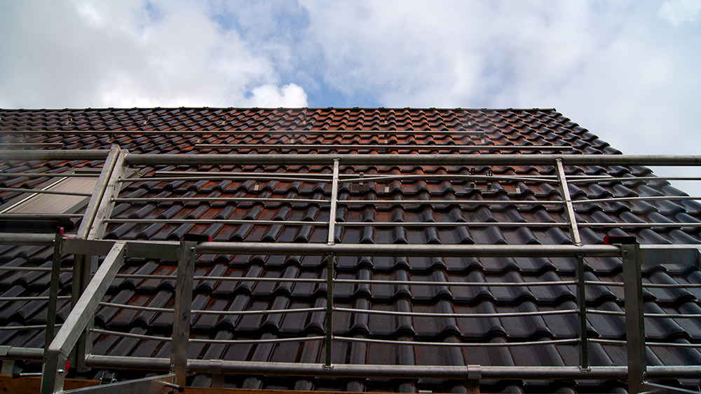 Dunkles Hausdach von unten fotografiert. Im Vordergrund sieht man den Fallschutz für die Handwerker, die eine Solaranlage auf dem Dach installieren.