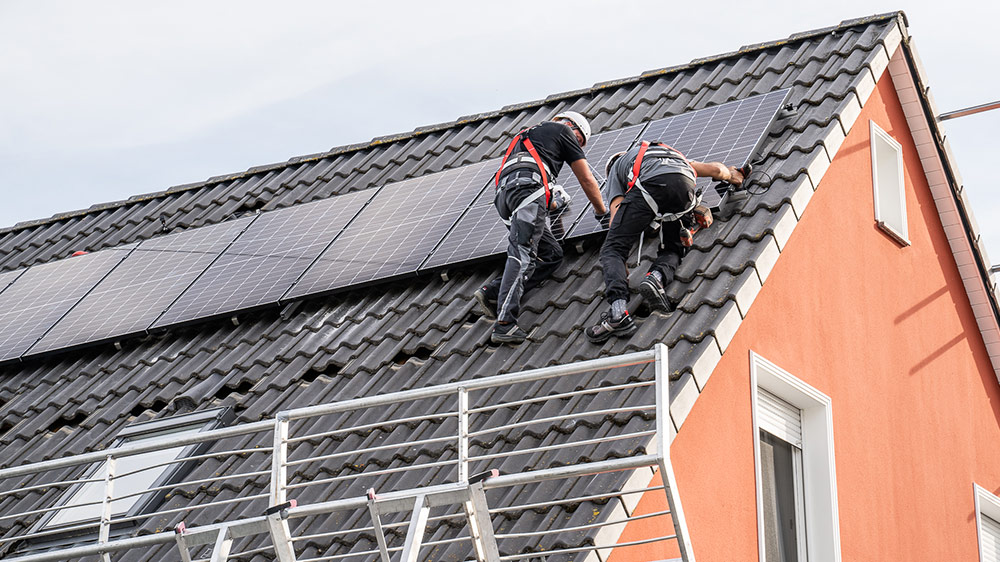 Zwei Infravoltaic Solar-Monteure bei der Installation einer Solaranlage. Sie befestigen ein Solarmodul an den Montageschienen.
