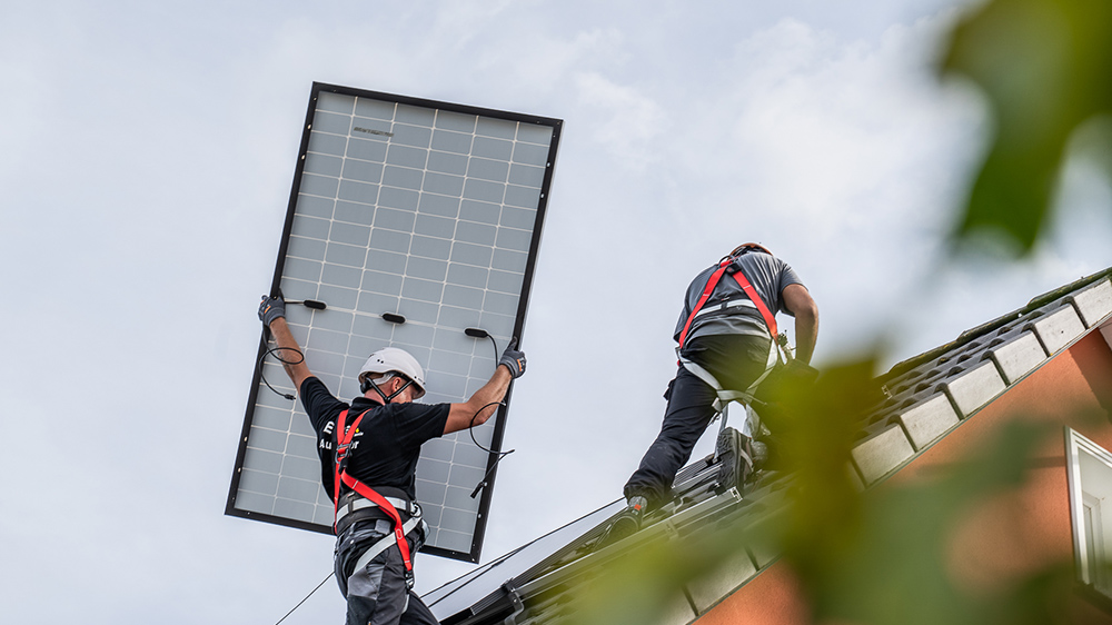 Zwei Infravoltaic Handwerker bei der Montage einer Solaranlage. Ein Monteur hält ein Modul mit beiden Händen so in der Hand, dass man die Rückseite sehen kann