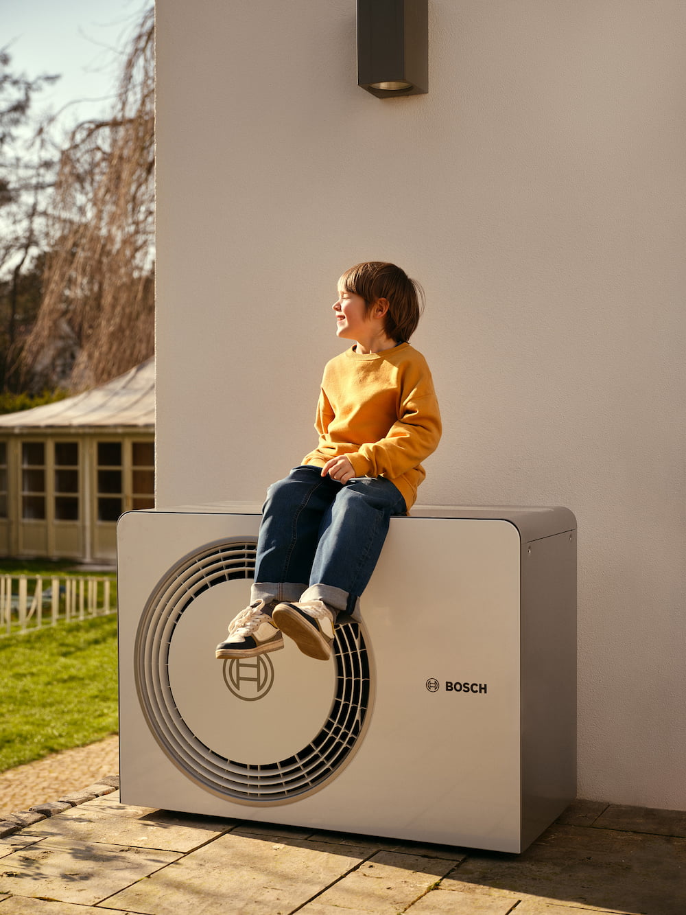 Junge sitzt auf Infravoltaic Wärmepumpe vor einer Hauswand
