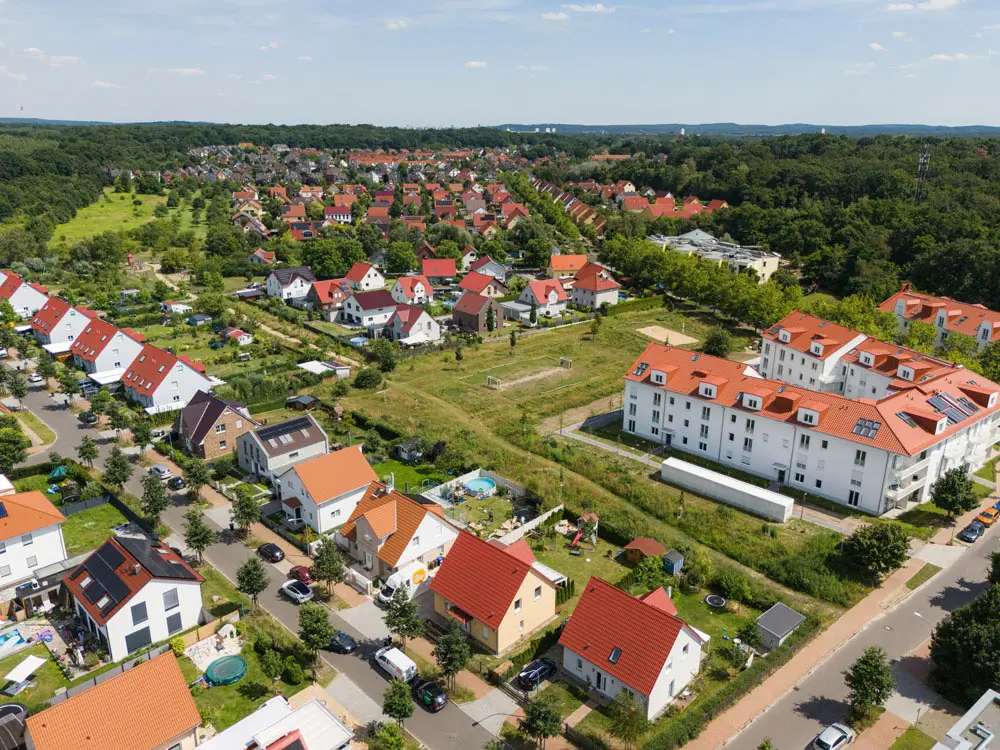 Ein Hausdach mit hellbraunen Ziegeln aus der Vogelperspektive, während eine Solaranlage installiert wird. Man sieht das Montagegerüst, die Montageschienen, zwei Handwerker auf dem Dach und einige fertig montierte Solarmodule.