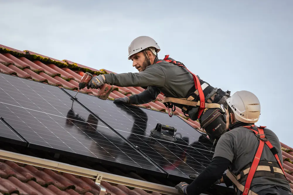 Zwei Infravoltaic Handwerker befestigen Solarmodule auf einem Hausdach.